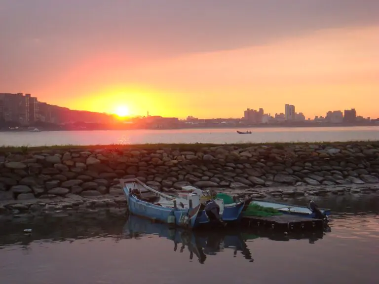 Fishing boats by the stone embankment at Tamsui with the sun setting over the river mouth